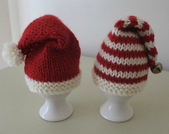 May include: Two knitted egg cozies, one red with a white pom-pom and the other red and white striped with a bell.