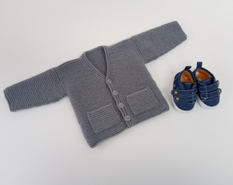 May include: A grey knitted cardigan with a V-neck, button fastening, and two patch pockets. The cardigan is laid flat on a white surface.  Next to the cardigan are two blue canvas shoes with yellow star accents.