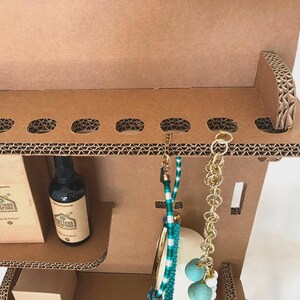 May include: A brown cardboard display unit with a perfume bottle, jewelry, and a box. The unit has oval cutouts and a shelf. The jewelry includes a gold chain and a turquoise beaded necklace. The perfume bottle has a brown label.