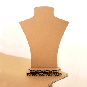 Op de afbeelding: Een bruine kartonnen buste voor het presenteren van kettingen. De buste is ontworpen om kettingen en hangers te presenteren. De display heeft een nek- en schoudervorm, met een gegolfde basis voor stabiliteit. De achtergrond is wit.