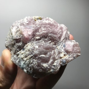 May include: A cluster of pink lepidolite crystals with a few blue kyanite crystals. The crystals are in a rough, natural state and have a translucent appearance.