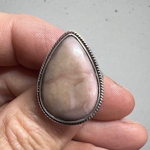 May include: A teardrop-shaped ring with a pink and white gemstone set in a silver bezel.