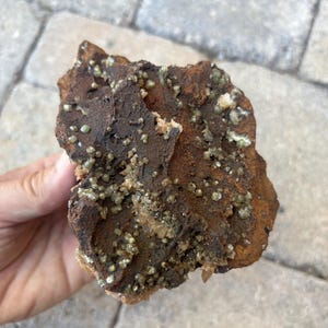 May include: A rough, brown rock with a cluster of small, green crystals embedded in its surface. The crystals are scattered throughout the rock, creating a visually interesting texture.