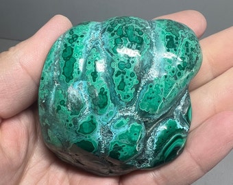 May include: A green and white malachite stone with a swirling, organic pattern. The stone is smooth and polished, and has a natural, earthy look.