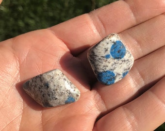 May include: Two tumbled stones with a white and gray speckled surface and blue spots.