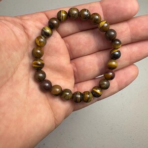 May include: A beaded bracelet featuring round, polished tiger's eye stones in shades of brown and gold. The bracelet is strung on an elastic band, showcasing the natural patterns and colors of the gemstones. A simple, elegant accessory.