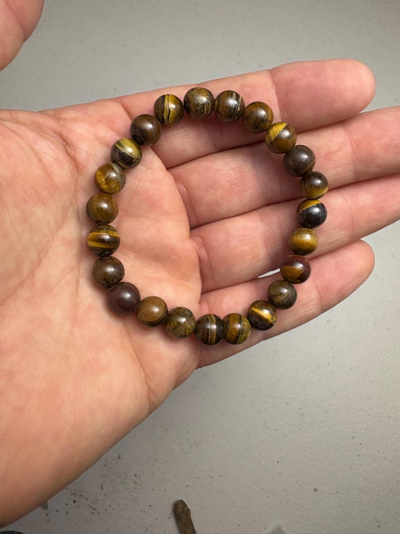 May include: A beaded bracelet featuring round, polished tiger's eye stones in shades of brown and gold. The bracelet is strung on an elastic band, showcasing the natural patterns and colors of the gemstones. A simple, elegant accessory.
