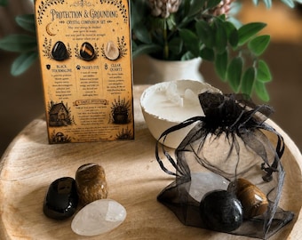 Puede incluir: Un conjunto de cristales Protection & Grounding con una tarjeta informativa rectangular, un cuenco blanco con una vela y tres piedras pulidas: turmalina negra, ojo de tigre y cuarzo claro, con duplicados en una bolsa de organza negra.