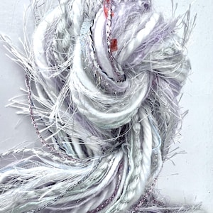 May include: A bundle of white, silver, and pink yarn with a frayed texture. The yarn is twisted and knotted together, creating a unique and textured look.