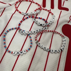 May include: Four beaded bracelets with white beads and red, blue, and white accents. The bracelets spell out "GO PHILS", "WET BANDITS", "JAWS", and "RING THE BELL" with a heart and a star charm.