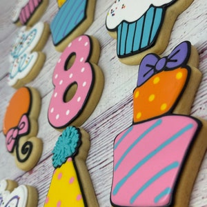 May include: A set of 12 decorated sugar cookies for an 8th birthday party. The cookies feature a variety of designs, including cupcakes, a number 8, a party hat, a gift box, and balloons. The cookies are decorated with colorful frosting and sprinkles.