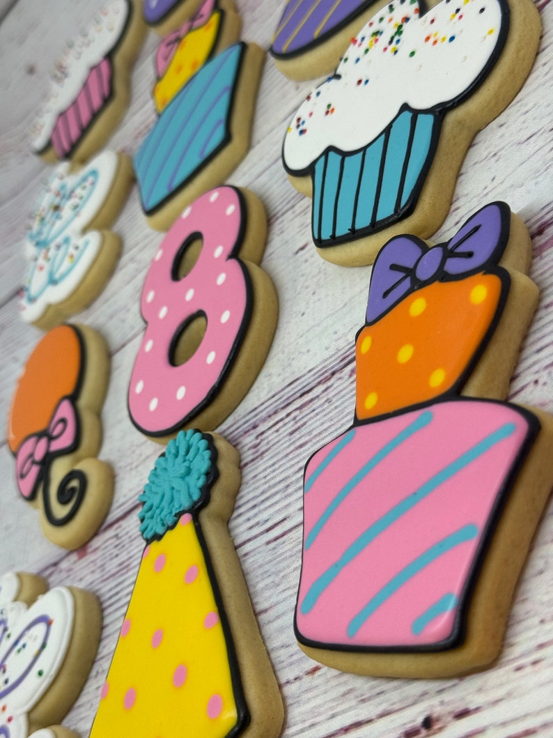 May include: A set of 12 decorated sugar cookies for an 8th birthday party. The cookies feature a variety of designs, including cupcakes, a number 8, a party hat, a gift box, and balloons. The cookies are decorated with colorful frosting and sprinkles.