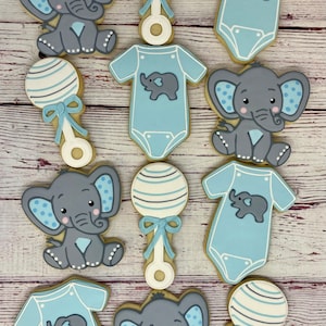 May include: A set of ten decorated sugar cookies featuring baby elephants and rattles. The cookies are decorated in shades of blue, gray, and white.