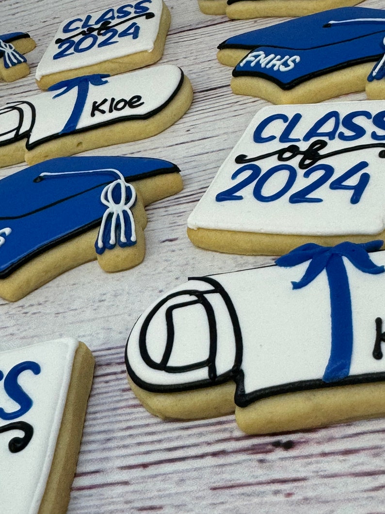May include: Assortment of graduation themed sugar cookies decorated with blue, black, and white icing. The cookies feature the text "Class of 2024", "FMHS", and "Kloe".