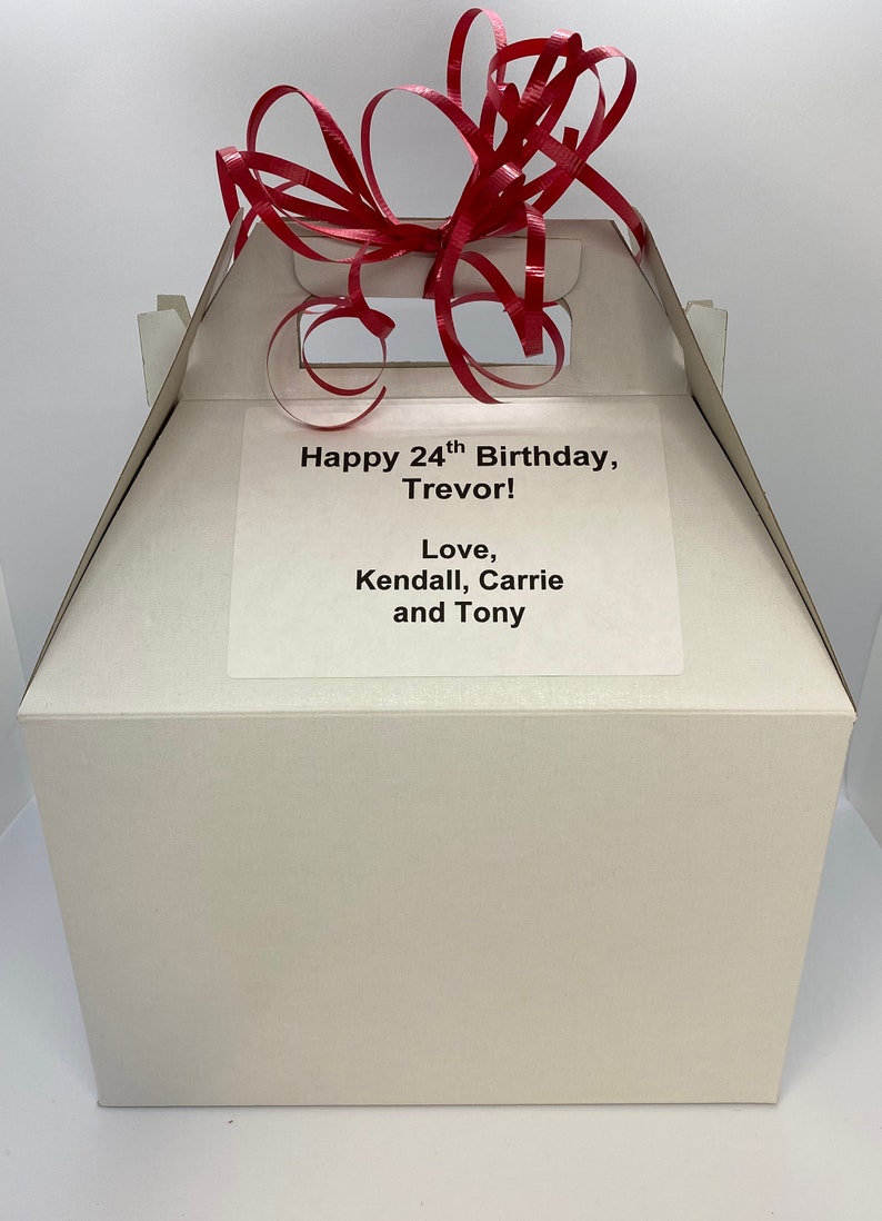 May include: A white gift box with a red ribbon on top. The box has a label that says "Happy 24th Birthday, Trevor! Love, Kendall, Carrie and Tony."