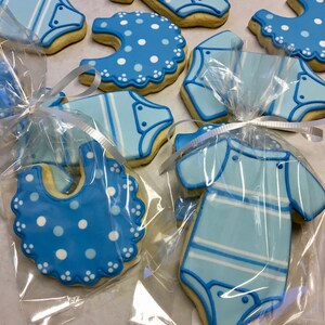 K&ouml;nnte beinhalten: Ein Set blauer und wei&szlig;er Babyparty-Kekse, verziert mit verschiedenen Baby-Motiven, darunter Strampler, L&auml;tzchen und Punkte. Die Kekse sind in durchsichtigen Plastikt&uuml;ten verpackt und bereit zum Verschenken.
