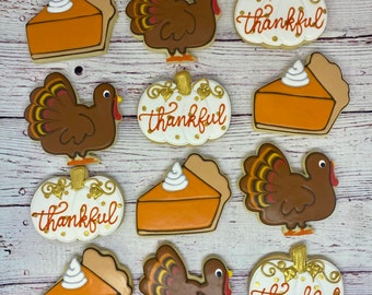 May include: Nine Thanksgiving-themed sugar cookies decorated with icing. The cookies feature images of turkeys, pumpkin pies, and pumpkins with the word "thankful" written on them.