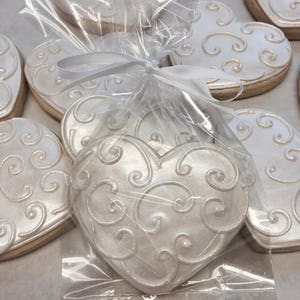 Puede incluir: Un paquete de galletas blancas en forma de coraz&oacute;n con un dise&ntilde;o de espiral. Las galletas est&aacute;n atadas con una cinta blanca y empaquetadas en una bolsa de pl&aacute;stico transparente.