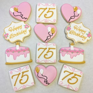 以下が含まれることがあります： ピンクとゴールドで飾られた砂糖菓子のセットです。クッキーはハート型、正方形、ケーキ型です。クッキーは数字の75、