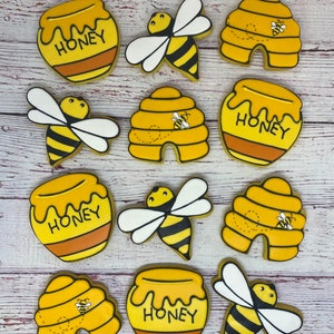 May include: A set of nine yellow and black bee-themed sugar cookies. The cookies are decorated with honey pots, beehives, and bees. The honey pots have the word "Honey" written on them.