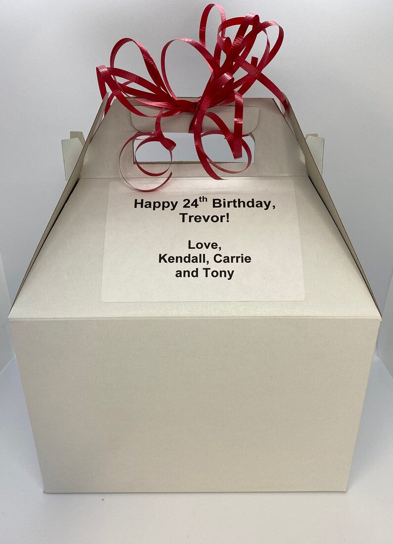 Puede incluir: Una caja de regalo blanca con una cinta roja en la parte superior. La caja tiene una etiqueta que dice "Happy 24th Birthday, Trevor! Love, Kendall, Carrie and Tony."