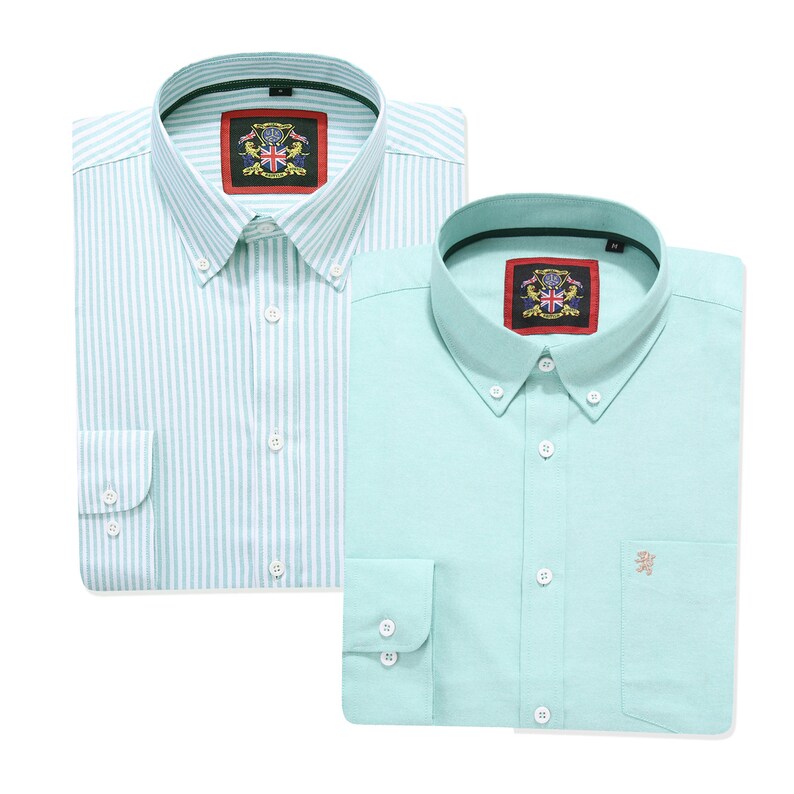 Puede incluir: Dos camisas de manga larga con botones. Una es de color verde claro con rayas verticales blancas y la otra es de color verde claro s&oacute;lido con un peque&ntilde;o emblema bordado en el bolsillo del pecho. Ambas tienen un cuello con una etiqueta roja.