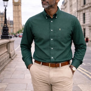 Peut inclure: Un homme porte une chemise vert fonc&eacute;, un pantalon beige et une ceinture en cuir marron. Il porte &eacute;galement une montre. L'arri&egrave;re-plan montre un b&acirc;timent historique et une tour d'horloge.