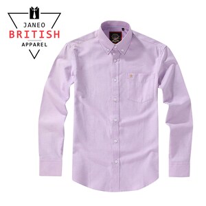 Puede incluir: Camisa lila claro de manga larga con cuello abotonado y bolsillo en el pecho. La camisa presenta un peque&ntilde;o emblema bordado en el bolsillo y el texto "JANEO BRITISH APPAREL" en un logotipo triangular.