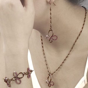 May include: A set of rose gold jewelry featuring a delicate butterfly design with pink crystals. The set includes a necklace, earrings, and a bracelet.