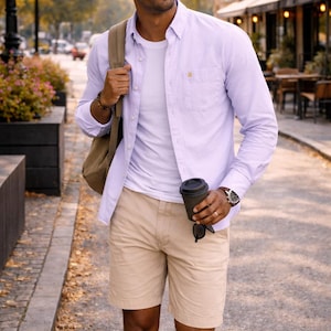 Puede incluir: Un hombre con una camisa lila clara, camiseta blanca y pantalones cortos color caqui, lleva una mochila y una taza de caf&eacute; negra. Lleva gafas de sol y un reloj. La imagen muestra un atuendo casual.