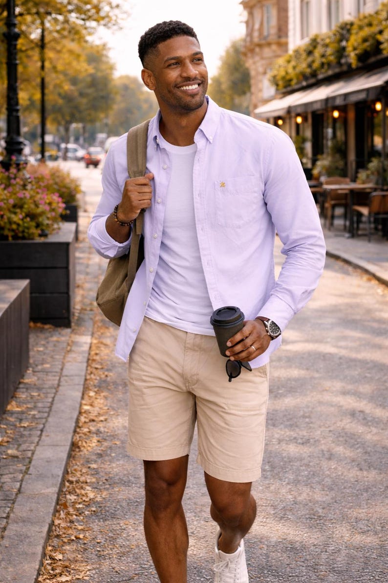 Puede incluir: Un hombre con una camisa lila clara, camiseta blanca y pantalones cortos color caqui, lleva una mochila y una taza de caf&eacute; negra. Lleva gafas de sol y un reloj. La imagen muestra un atuendo casual.