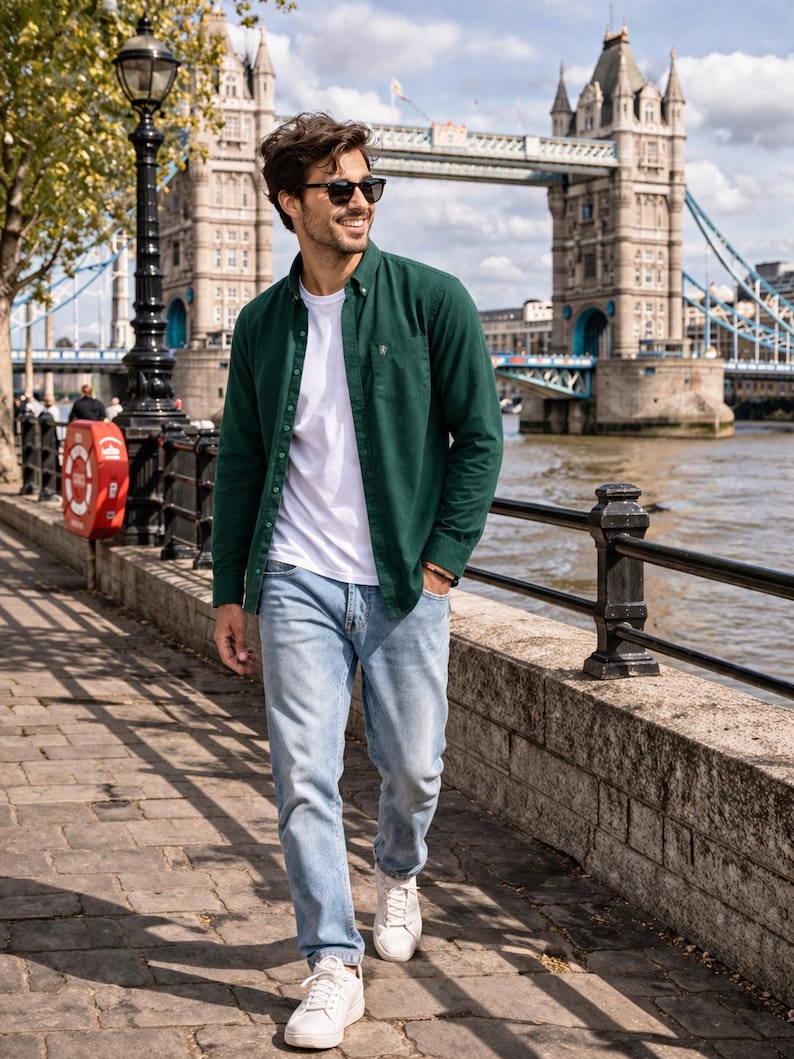 Peut inclure: Une personne v&ecirc;tue d'une chemise vert fonc&eacute;, d'un t-shirt blanc, d'un jean bleu clair et de baskets blanches. Le Tower Bridge de Londres est visible en arri&egrave;re-plan par une journ&eacute;e ensoleill&eacute;e.