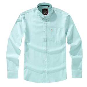 Puede incluir: Una camisa de manga larga en color verde menta claro con cuello abotonado, un bolsillo en el pecho con un peque&ntilde;o emblema bordado y una tapeta central con botones blancos. La prenda presenta un tejido con textura y un corte estructurado.