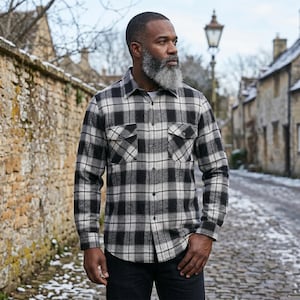 Puede incluir: Una camisa de manga larga con botones y un patrón de cuadros en negro, blanco y gris. La camisa incluye un cuello estándar, una tapeta frontal con botones y dos bolsillos en el pecho con solapas abotonadas. La tela tiene una textura suave.