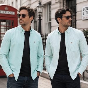 Puede incluir: Dos camisas de manga larga con botones sobre camisetas negras. Una camisa es de color verde menta claro liso y la otra presenta un patr&oacute;n de rayas verticales en verde menta claro y blanco. Ambas tienen un peque&ntilde;o le&oacute;n dorado bordado en el pecho.