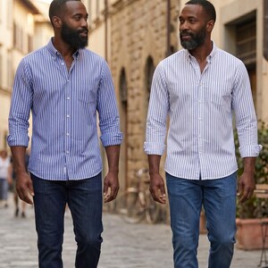 Op de afbeelding: Twee mannen in gestreepte overhemden met knopen en donkerblauwe jeans. E&eacute;n overhemd is blauw en wit, de andere is wit en blauw. De overhemden hebben lange mouwen en zijn dichtgeknoopt. Ze lopen op een geplaveide straat.