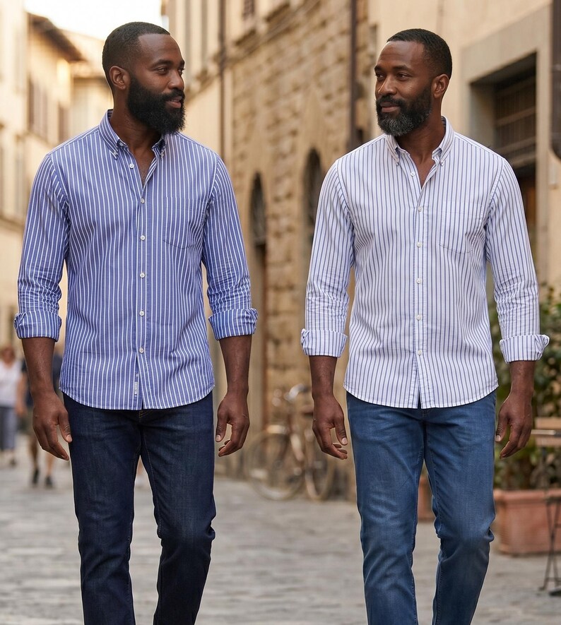 Op de afbeelding: Twee mannen in gestreepte overhemden met knopen en donkerblauwe jeans. E&eacute;n overhemd is blauw en wit, de andere is wit en blauw. De overhemden hebben lange mouwen en zijn dichtgeknoopt. Ze lopen op een geplaveide straat.