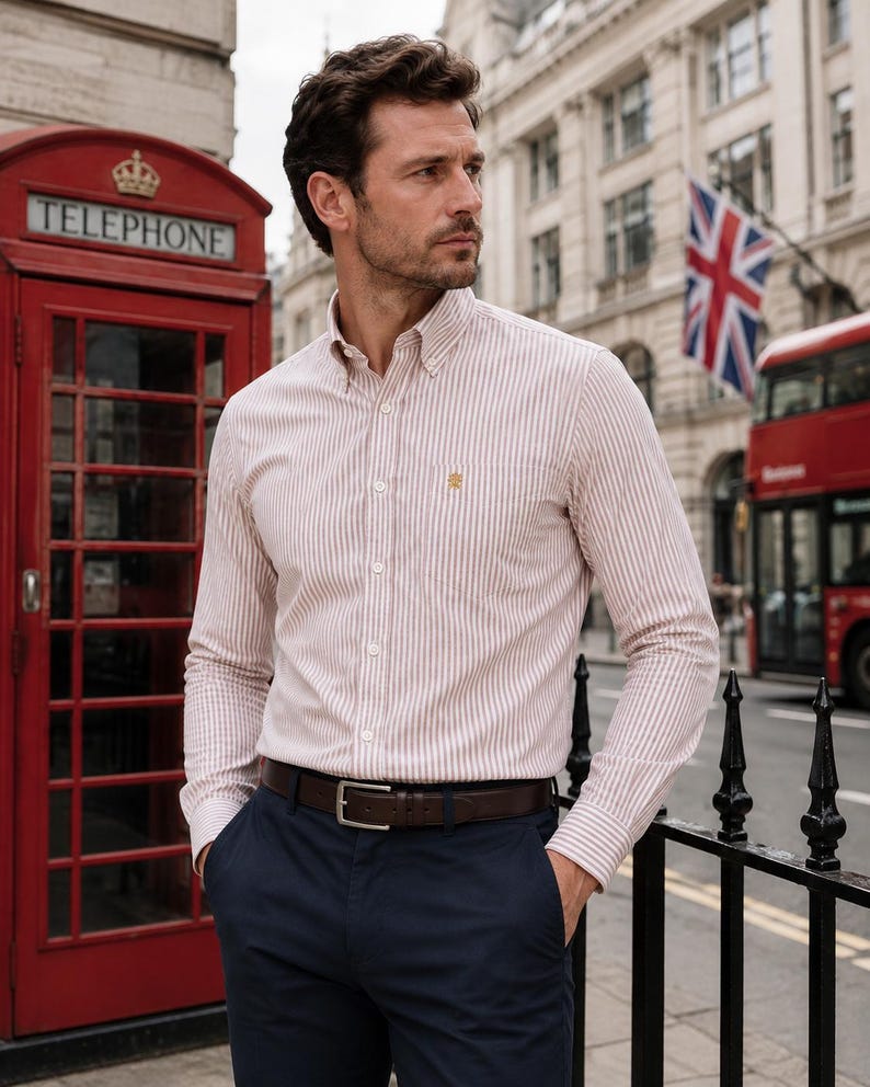 Puede incluir: Una camisa de manga larga con botones y un patr&oacute;n de rayas verticales en blanco y beige, con cuello abotonado, un bolsillo en el pecho con un peque&ntilde;o logotipo bordado y una tapeta frontal, combinada con pantalones azul marino oscuro.