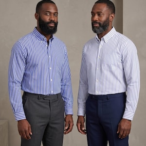 Op de afbeelding: Twee overhemden met verticale strepen. E&eacute;n overhemd is blauw en wit, de andere wit en blauw. Beide overhemden hebben lange mouwen en worden gecombineerd met een pantalon. E&eacute;n broek is grijs, de andere marineblauw.