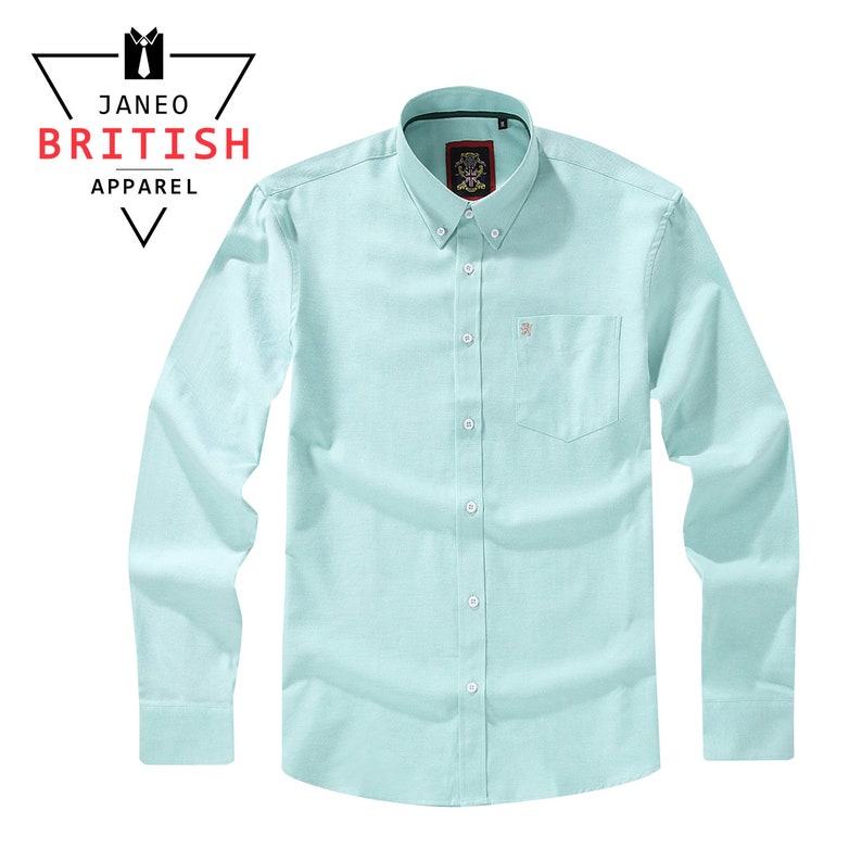 May include: A light blue button-down shirt with long sleeves and a chest pocket. The shirt has a small embroidered logo on the pocket and the brand name "JANEO BRITISH APPAREL" is displayed in the upper left corner.