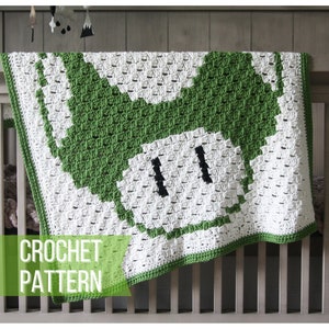 May include: Green and white crochet baby blanket with a pixelated mushroom design. The blanket is draped over a cot and says "CROCHET PATTERN" at the bottom.
