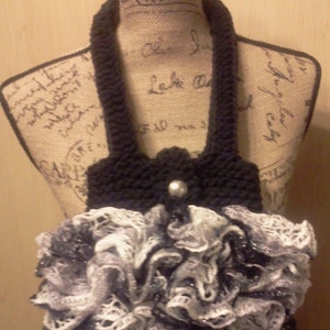 May include: A black crocheted bag with a ruffled white and black trim. The bag is on a mannequin with a burlap fabric covering.
