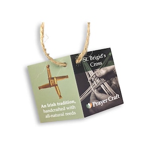 May include: A green and brown St. Brigid's Cross made of natural reeds. The cross is handcrafted and comes with a twine hanger. The tag reads "St. Brigid's Cross" and "An Irish tradition, handcrafted with all-natural reeds" and "Prayer Craft".