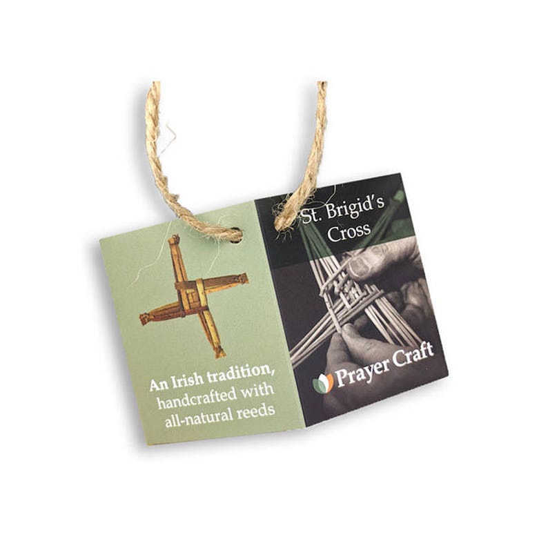 May include: A green and brown St. Brigid's Cross made of natural reeds. The cross is handcrafted and comes with a twine hanger. The tag reads "St. Brigid's Cross" and "An Irish tradition, handcrafted with all-natural reeds" and "Prayer Craft".
