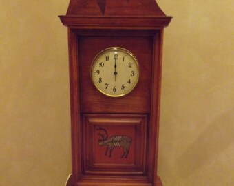 May include: A wooden clock with a mountain-shaped top and a reindeer design on the front. The clock face has black Roman numerals and a white background.