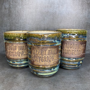 May include: Three ceramic mugs with a brown glaze and blue and green accents. Each mug has the text "About That Polygraph..." written on the front.