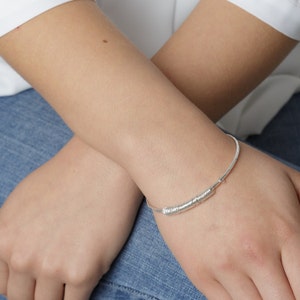 Puede incluir: Un brazalete de plata con un dise&ntilde;o trenzado. El brazalete se lleva en la mu&ntilde;eca.