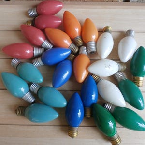 Peut inclure: Un assortiment d'ampoules de Noël vintage de différentes couleurs, dont rouge, orange, bleu, blanc, turquoise et vert. Les ampoules ont des bases argentées et sont disposées sur une surface en bois.