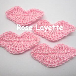 Op de afbeelding: Vier roze gecrochete lippen, elk in de vorm van een hart, zijn gerangschikt op een witte achtergrond. De tekst "Rose Layette" is zichtbaar in het midden van de afbeelding.