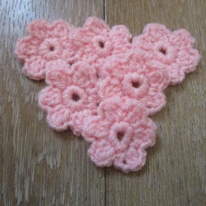 Peut inclure: Six fleurs crochetées roses disposées en forme de cœur. Les fleurs sont faites avec un fil doux et texturé.